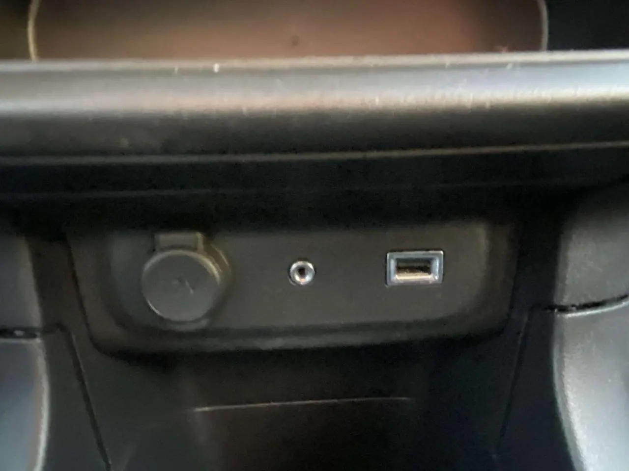 Gros plan sur les ports USB, prise jack et allume-cigare dans la console centrale d'une Citroën C3 noire toit rouge.