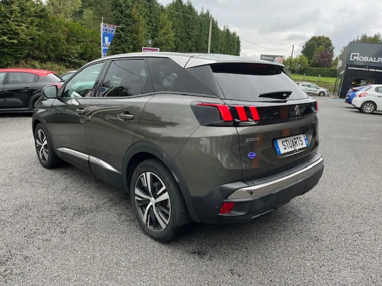 Peugeot 3008 gris Amazonite vue 3/4 arrière droit, jantes alliage et feux arrière à griffes rouges visibles.
