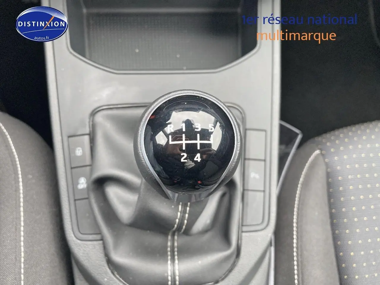 Gros plan sur le levier de vitesse manuel noir de la SEAT Ibiza 1.0 TSI 95 Copa, avec coutures blanches et sièges tissu gris à pois.