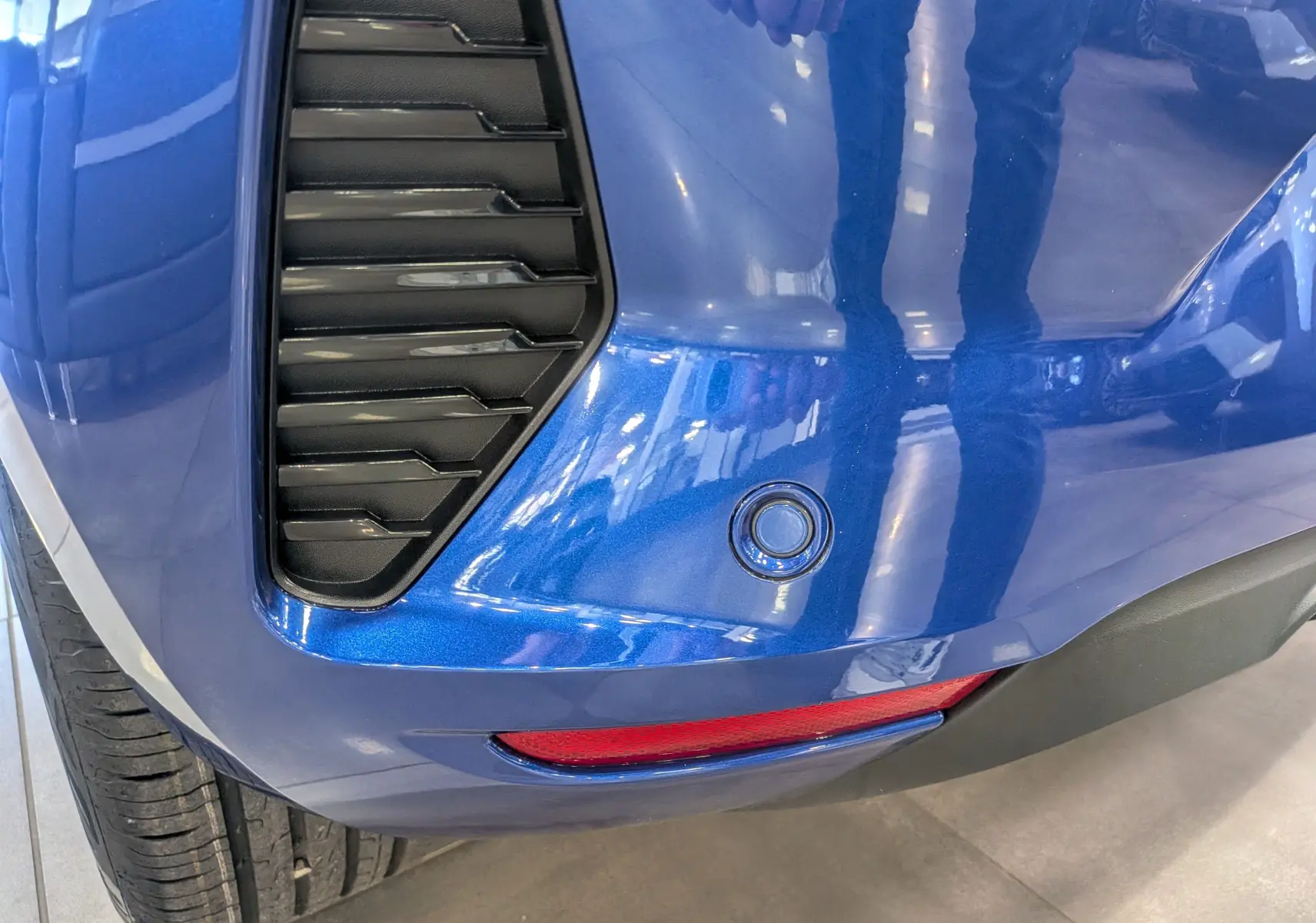 Détail du pare-chocs arrière bleu Iron de la Renault Clio V avec capteur de recul et feu rouge intégré, vue côté gauche.