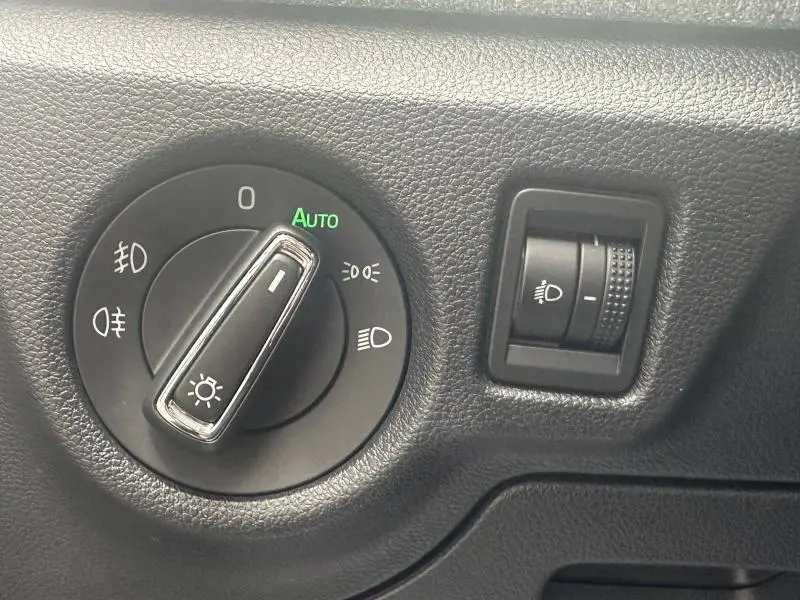 Gros plan sur la commande des phares et le réglage d’intensité lumineuse dans l’habitacle noir d’une Skoda Scala blanche.