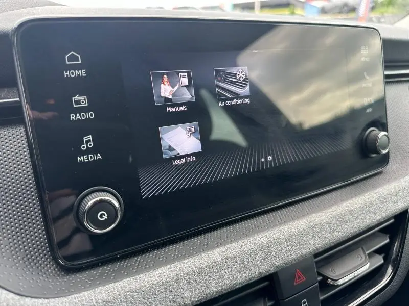 Écran tactile central en gros plan dans l’habitacle du Skoda Scala blanc, affichant les menus d’aide et climatisation.