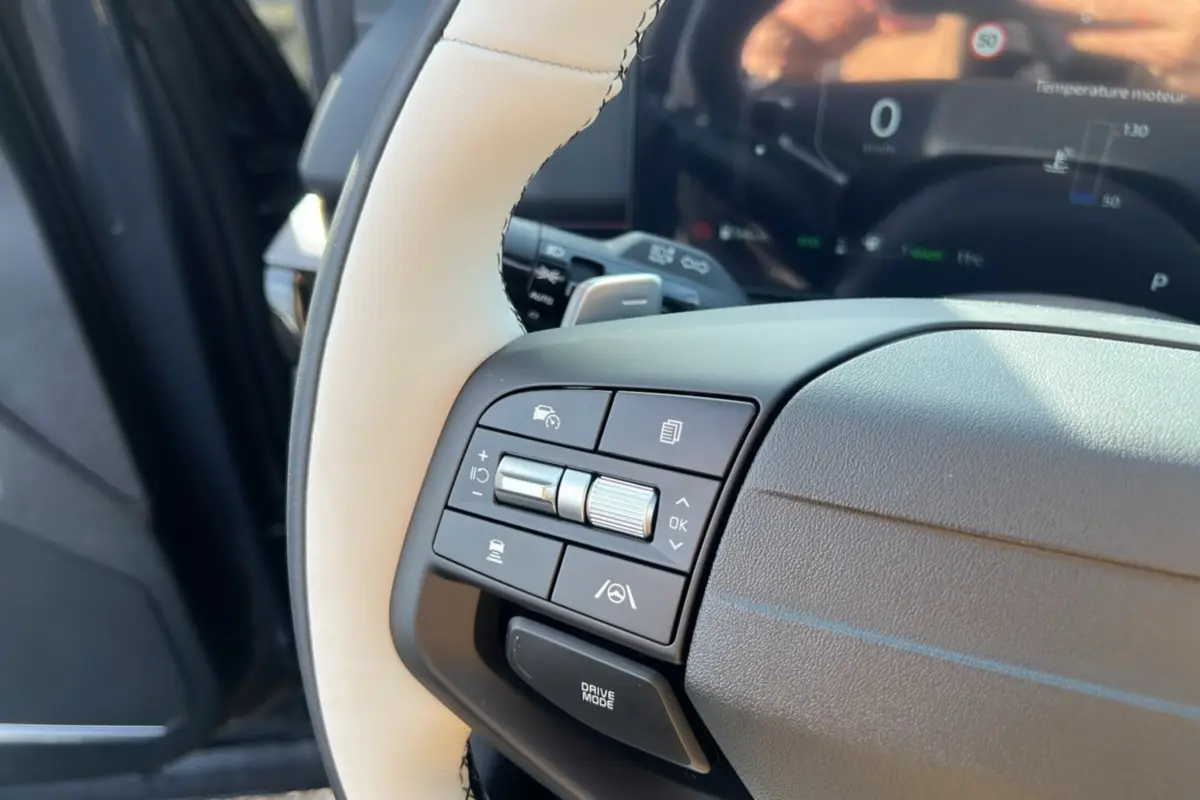 Gros plan sur le volant cuir beige du Kia Sportage 2026 avec commandes multifonctions côté gauche et tableau de bord numérique flou.