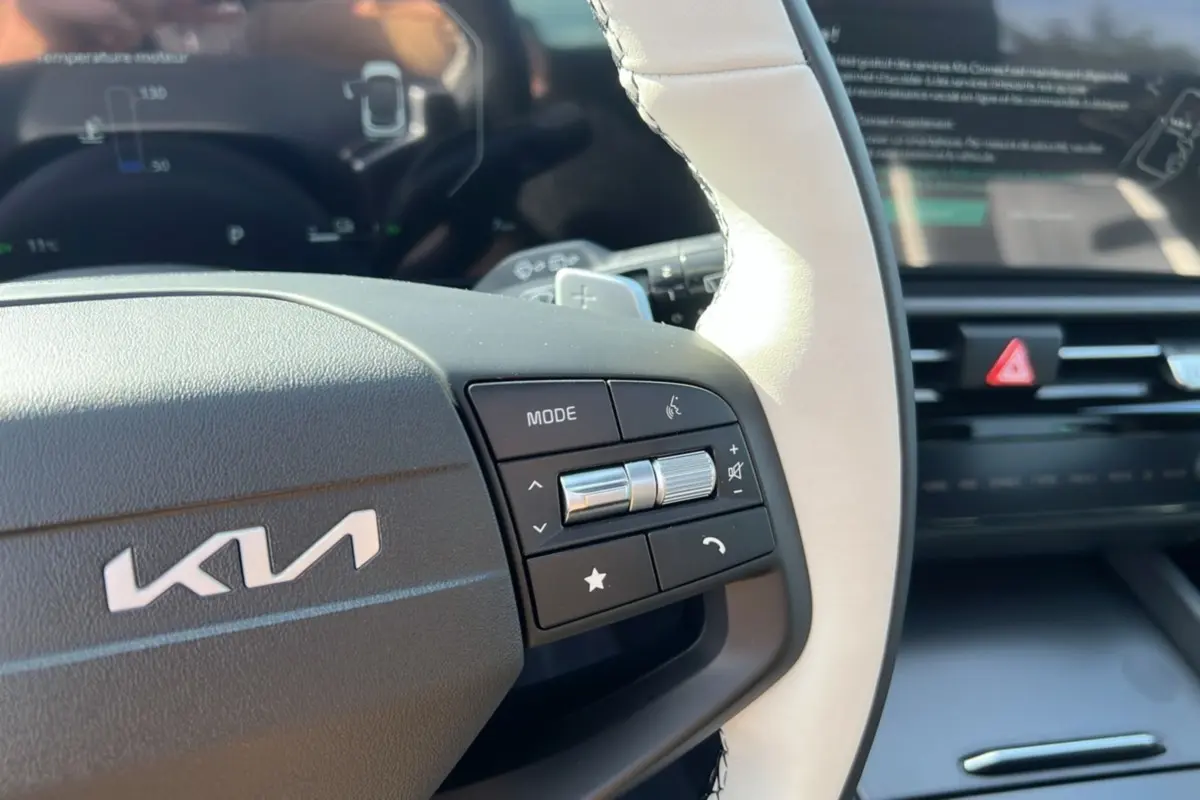Gros plan sur le volant cuir blanc de la Kia Sportage 2026 avec commandes multifonctions et tableau de bord numérique flou.