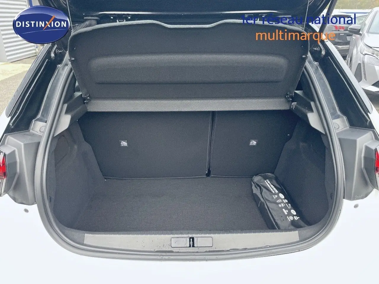 Coffre ouvert vu de l'arrière d'une Opel Corsa blanche 2022, avec un kit de sécurité noir dans le coffre.