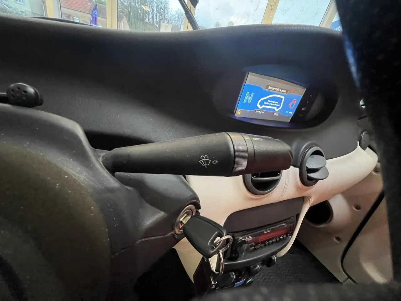 Vue rapprochée du tableau de bord beige et noir du Citroën E-MEHARI cabriolet 2016 avec clé insérée et écran digital allumé.