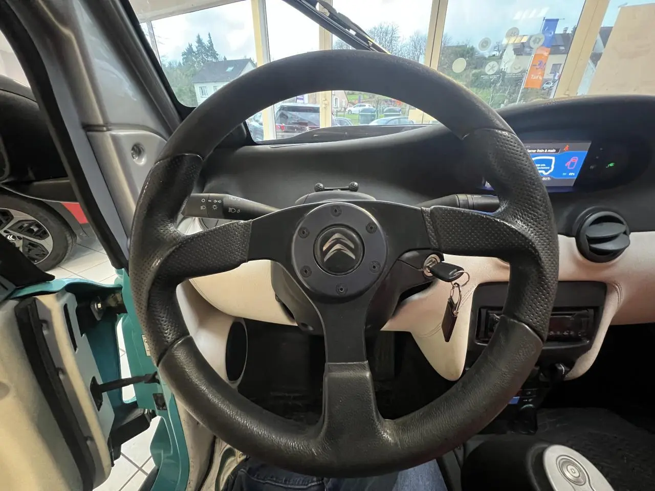 Vue intérieure centrée sur le volant noir du Citroën E-MEHARI cabriolet bleu clair avec tableau de bord et clé sur contact.