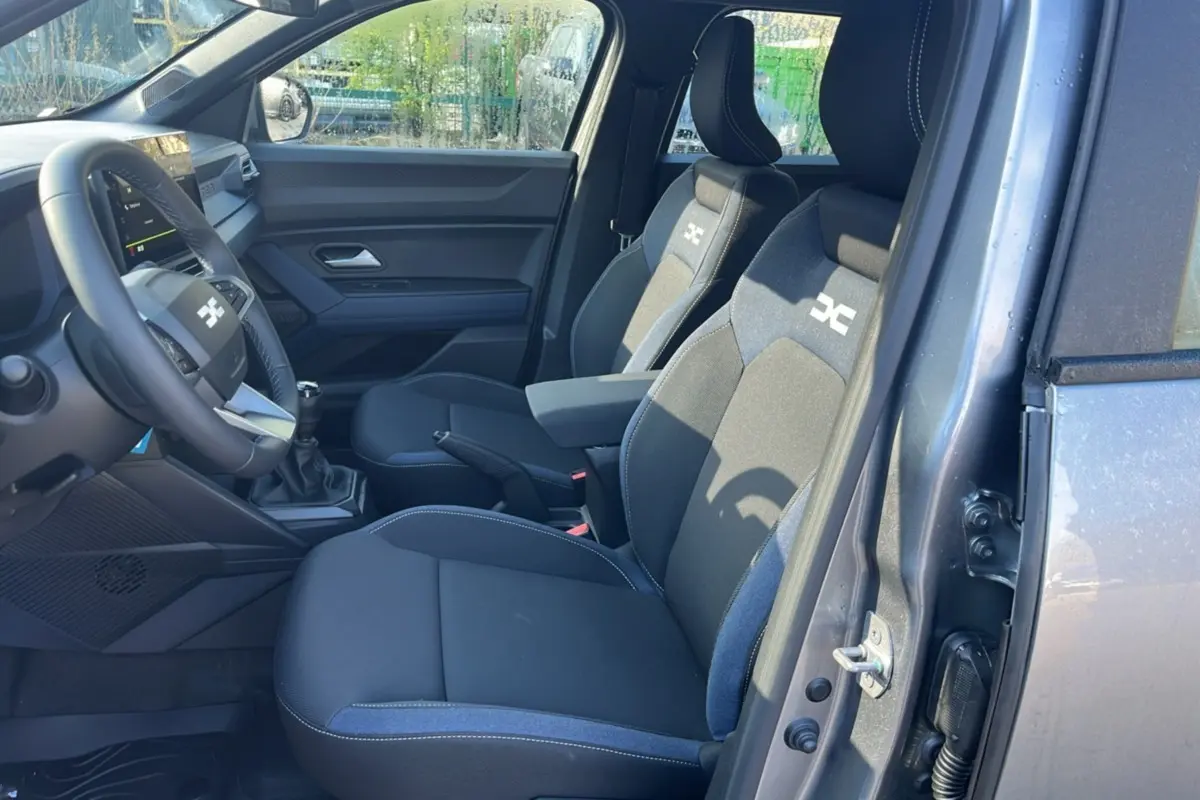 Vue intérieure côté conducteur du Dacia Duster 2025 gris schiste, montrant les sièges avec logo Expression et levier de vitesses manuel.