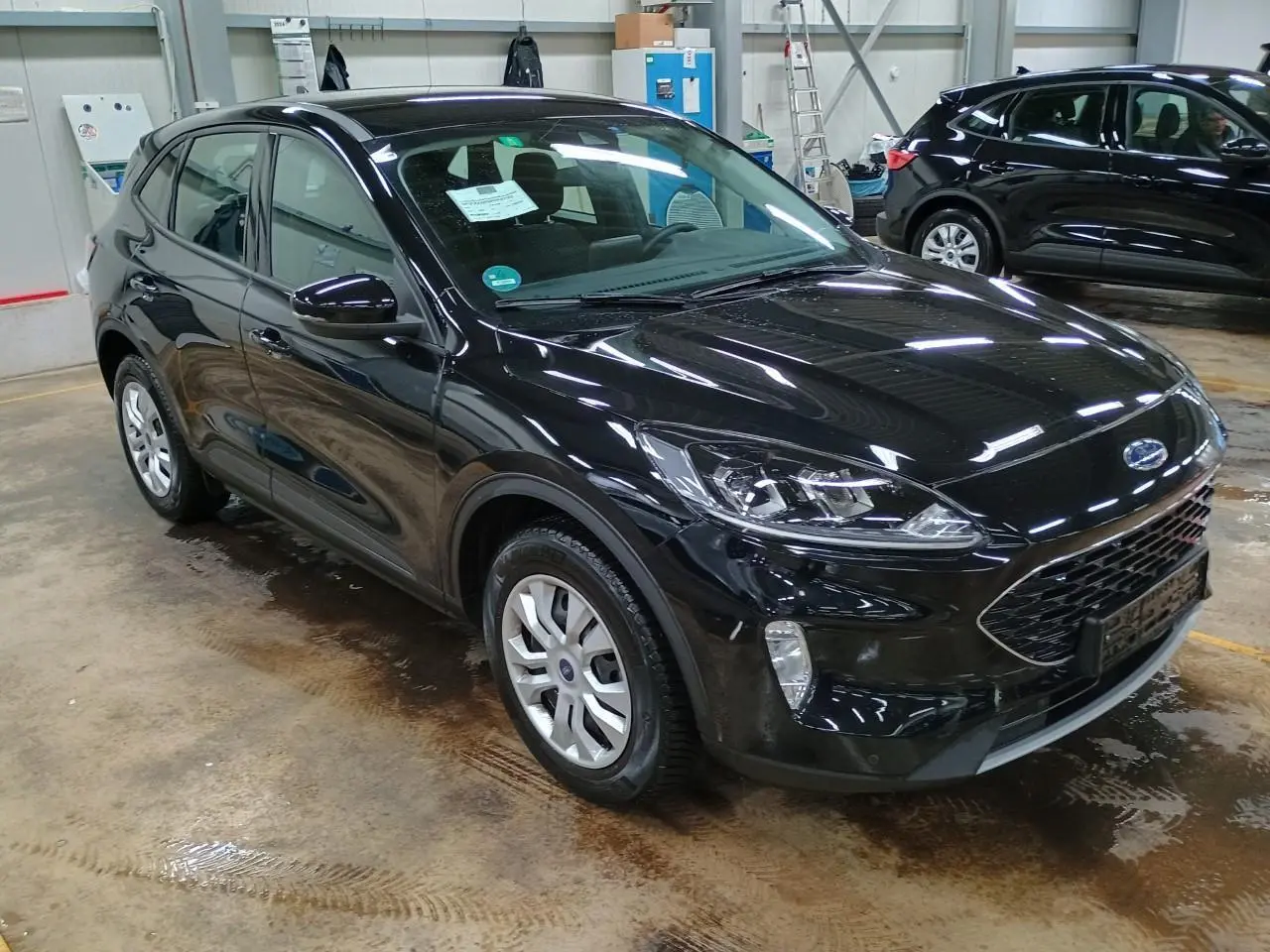 Ford Kuga noir Obsidien vu en 3/4 avant droit dans un garage, avec calandre et phares distinctifs visibles.