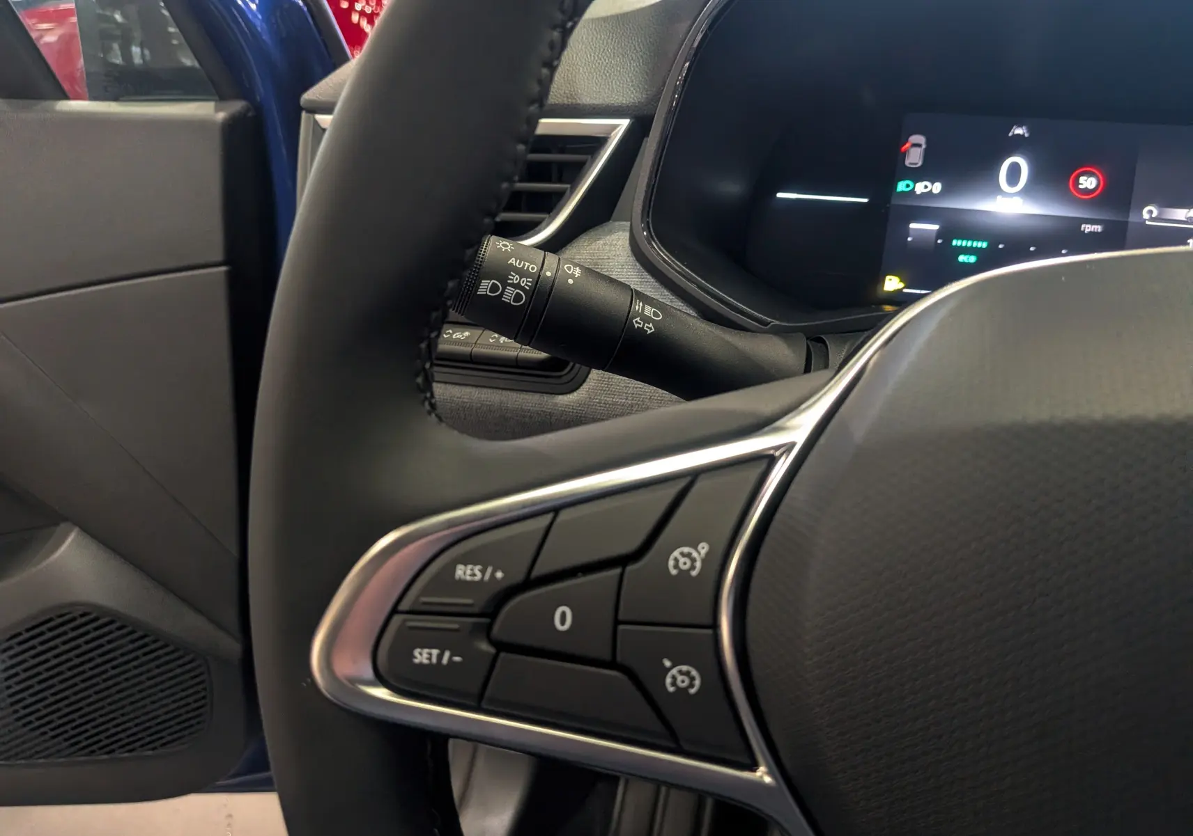 Gros plan sur le volant de la Renault Clio V Bleu Iron, montrant les commandes de régulateur de vitesse et l'écran digital.