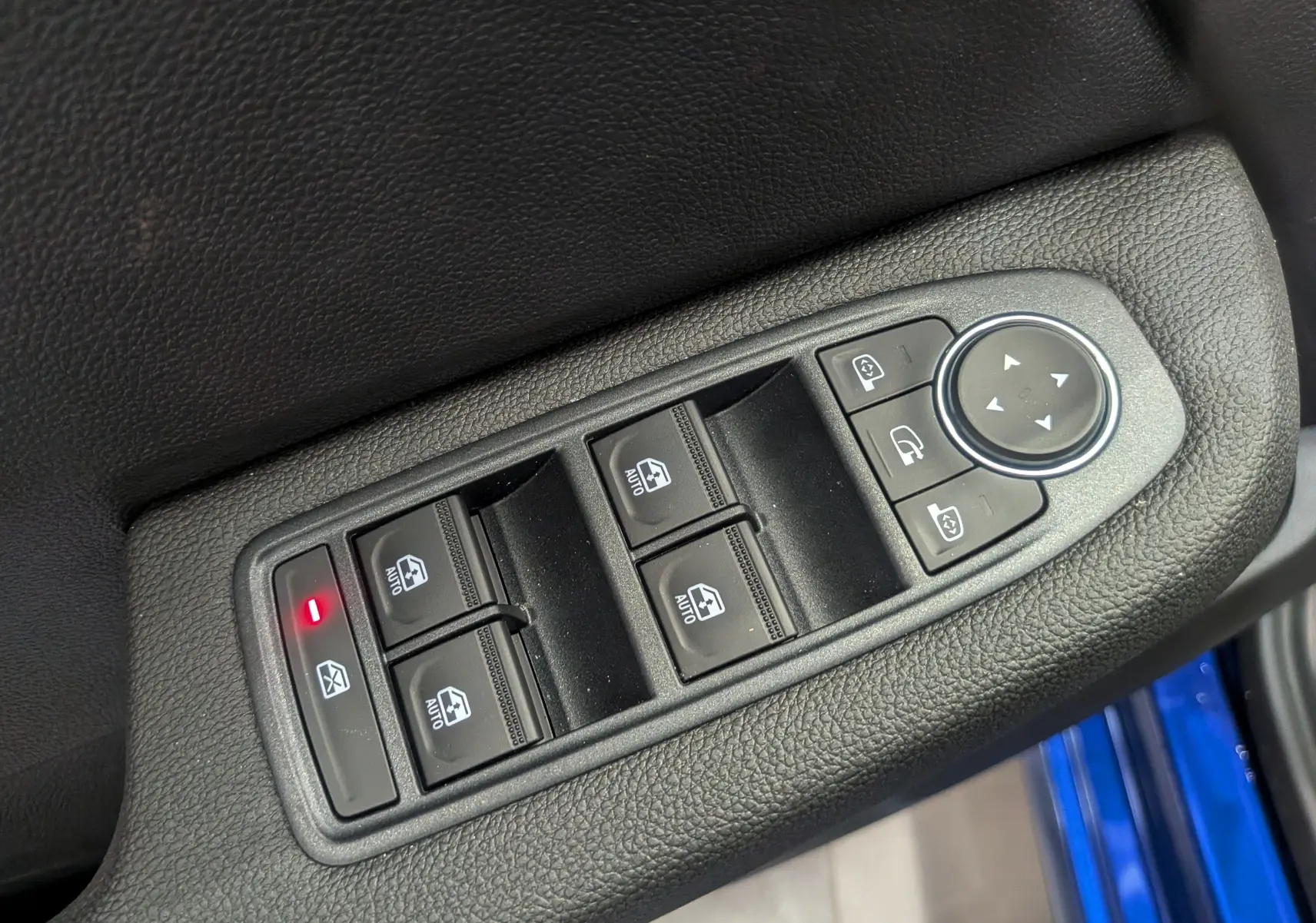 Gros plan sur les commandes de lève-vitres et rétroviseurs côté conducteur d’une Renault Clio V Bleu Iron, intérieur noir.