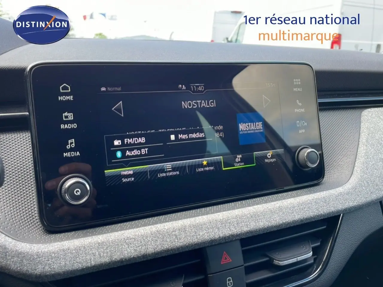 Écran tactile central du tableau de bord du Skoda Scala blanc glacier, affichant la radio Nostalgie en mode FM/DAB.