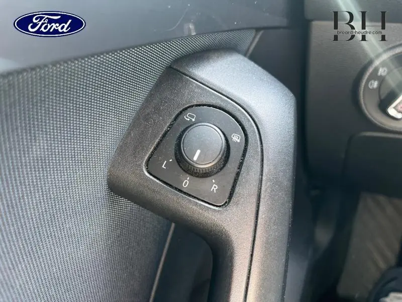 Gros plan sur le bouton de réglage des rétroviseurs côté conducteur, plastique noir texturé.