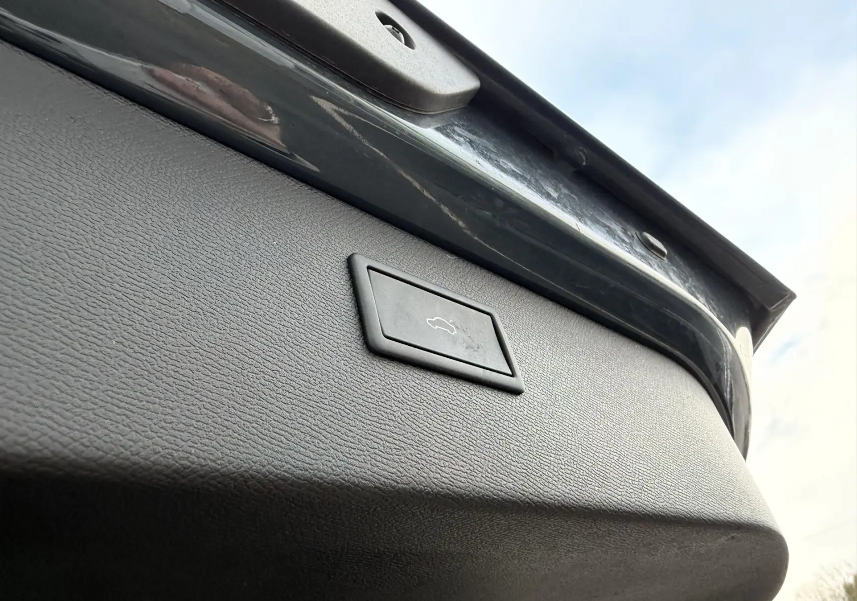 Gros plan sur le bouton d'ouverture du hayon électrique du coffre d'un CUPRA Formentor bleu, vue depuis l'arrière vers le haut.