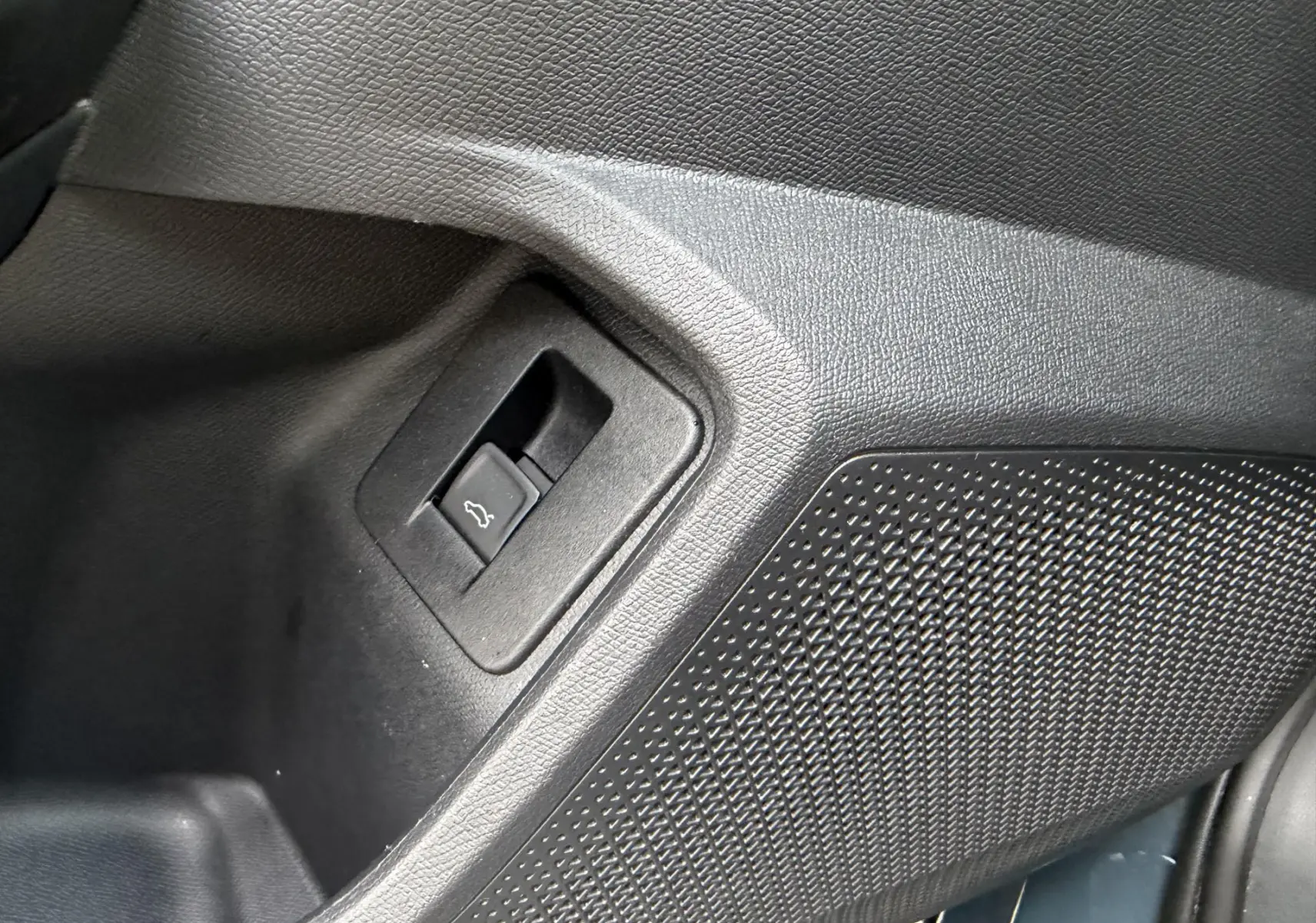 Détail intérieur du bouton d'ouverture du hayon dans un panneau noir texturé du CUPRA Formentor bleu 2025.