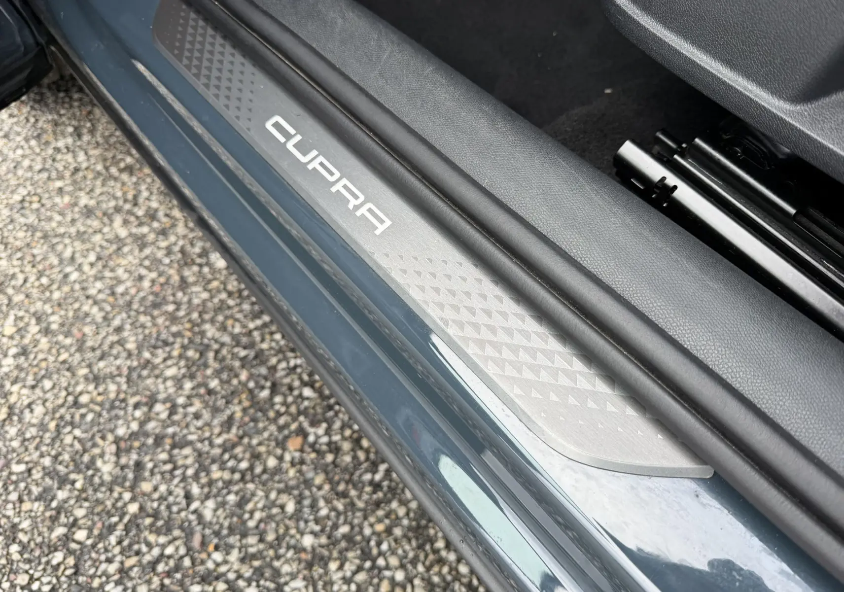 Gros plan sur la plaque de seuil de porte côté gauche bleu métallisé avec logo CUPRA blanc visible.