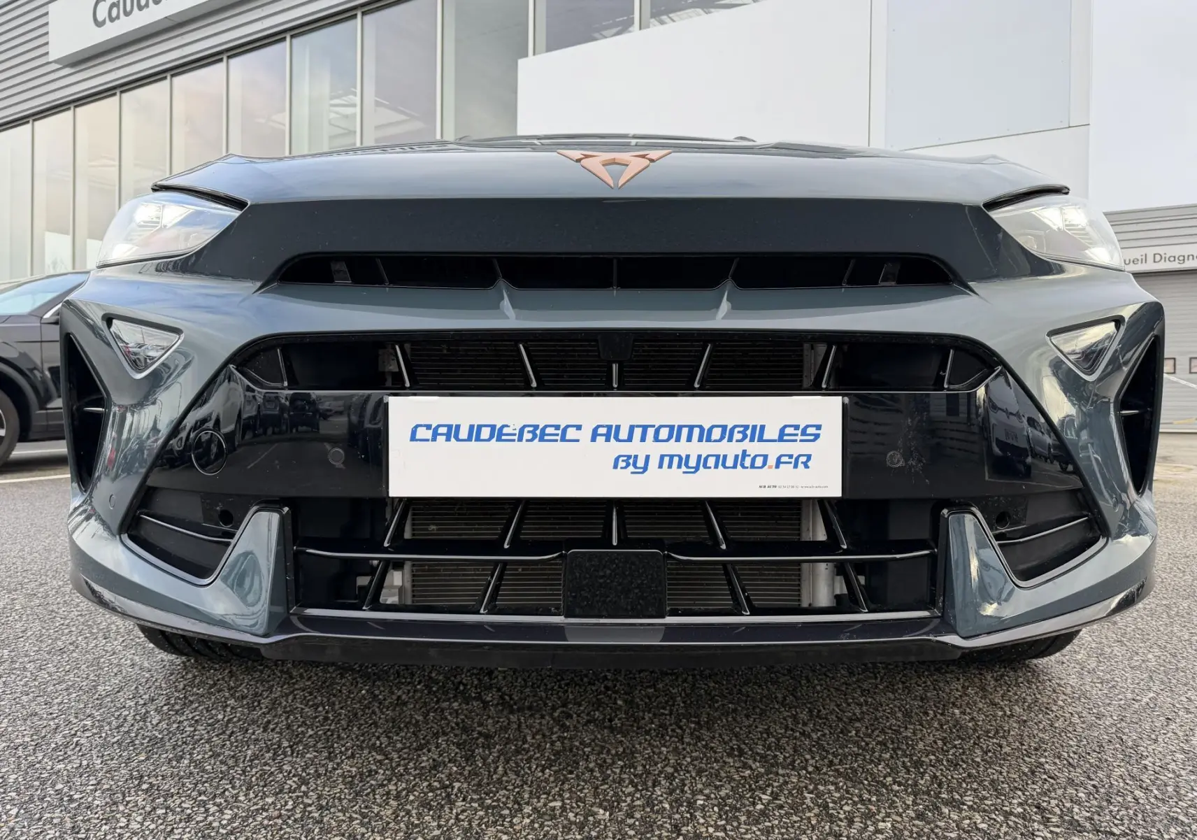 Vue frontale rapprochée de la CUPRA Formentor bleue avec logo cuivré et calandre large noire brillante.