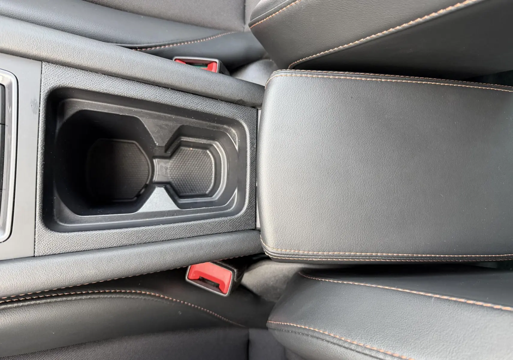 Gros plan sur la console centrale noire avec porte-gobelets et accoudoirs en cuir noir surpiqué orange du CUPRA Formentor.