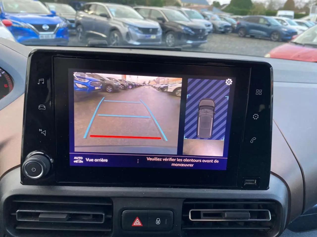 Écran de caméra de recul du Peugeot Rifter GT bleu montrant l'arrière et l'angle mort en parking extérieur.