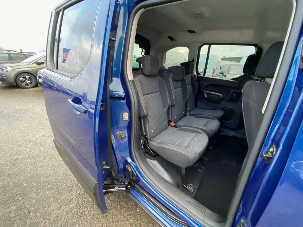 Vue latérale gauche du Peugeot Rifter GT bleu 2023, porte coulissante ouverte montrant les sièges arrière en tissu gris.