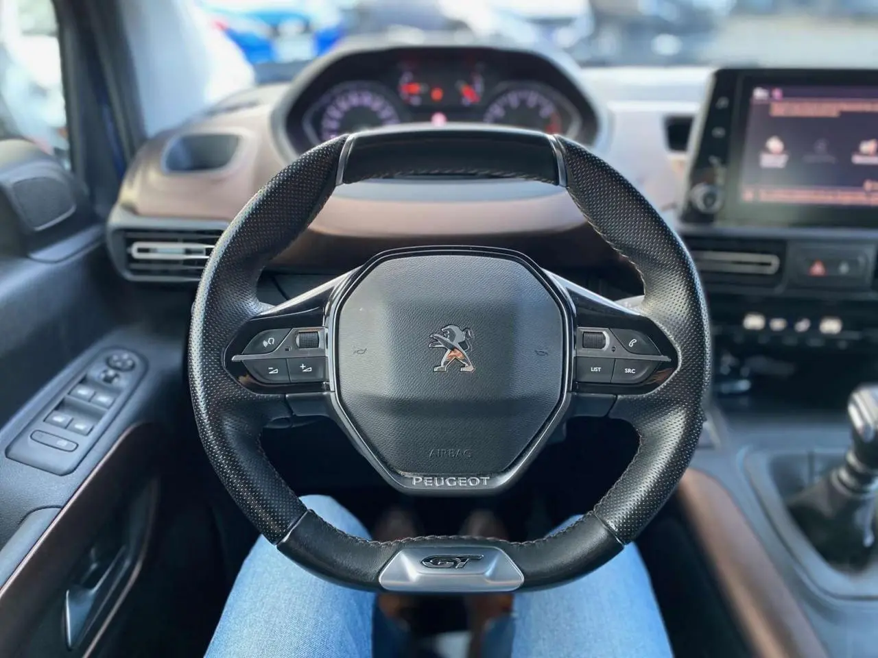 Volant GT noir en cuir avec logo Peugeot, vue centrée depuis le siège conducteur du Rifter bleu 2023.