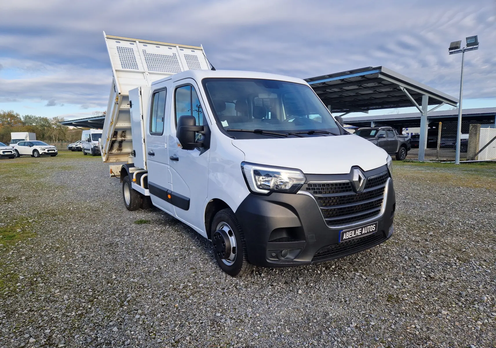 Renault Master blanc en 3/4 avant droit avec benne relevée et cabine double sur parking extérieur.