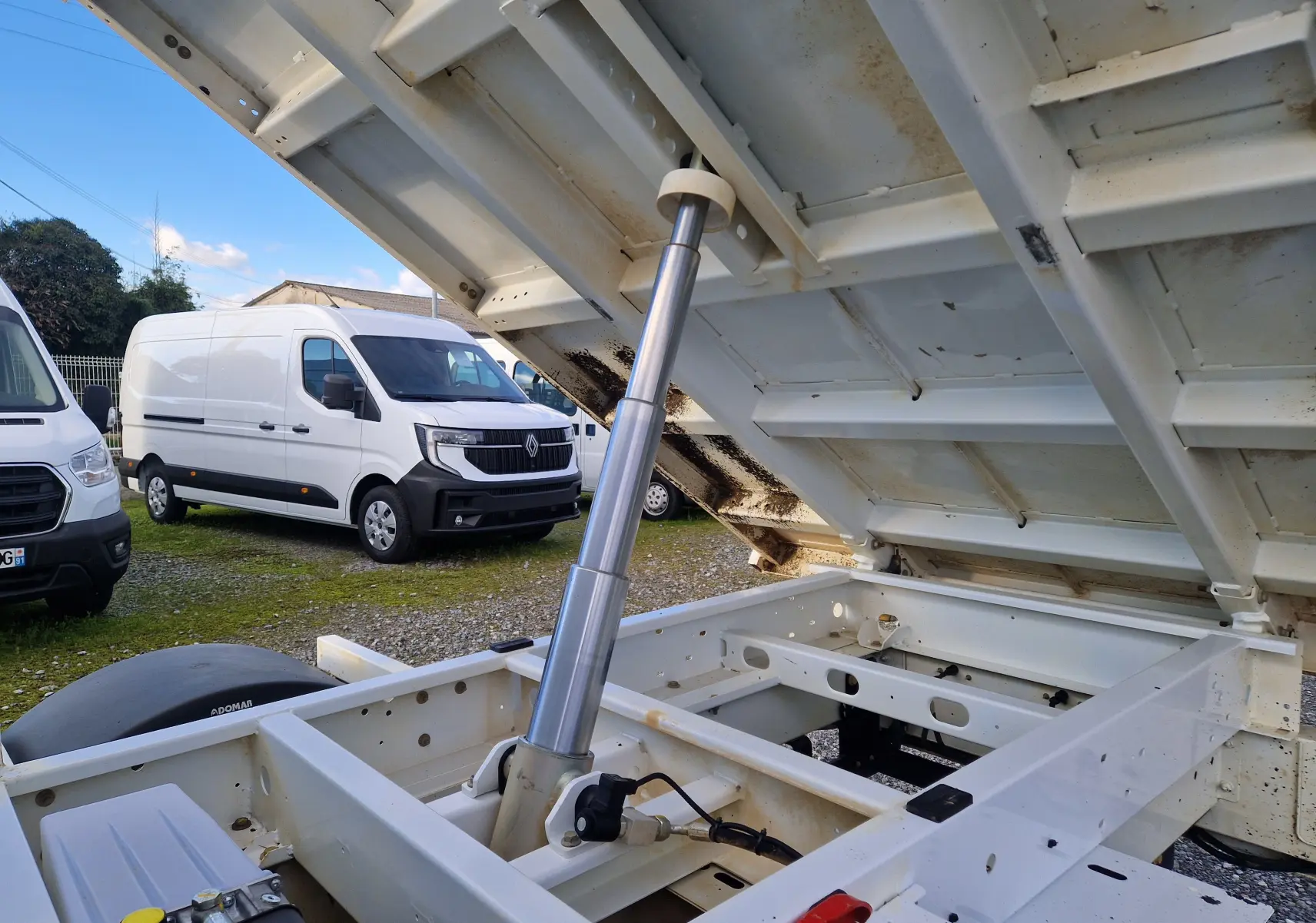 Vue arrière droite rapprochée du système de benne relevée d’un Renault Master blanc avec roues jumelées visibles.