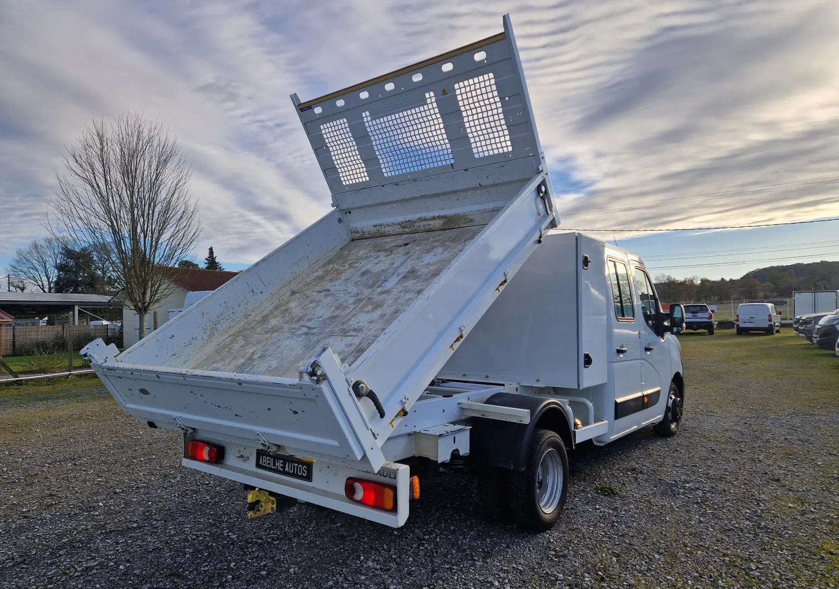 Vue 3/4 arrière droite du Renault Master blanc avec benne relevée et coffre latéral sur terrain extérieur.