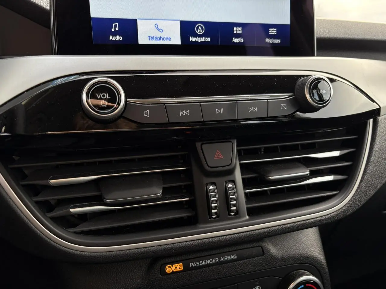 Détail de la console centrale du Ford Kuga 2024 avec commandes audio, ventilation et écran tactile affichant le menu navigation.