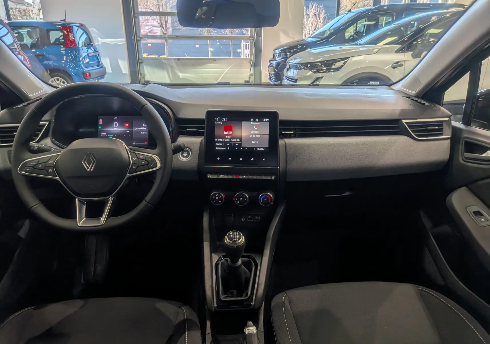 Vue intérieure avant de la Renault Clio V 2025, tableau de bord moderne avec écran tactile et volant multifonction.