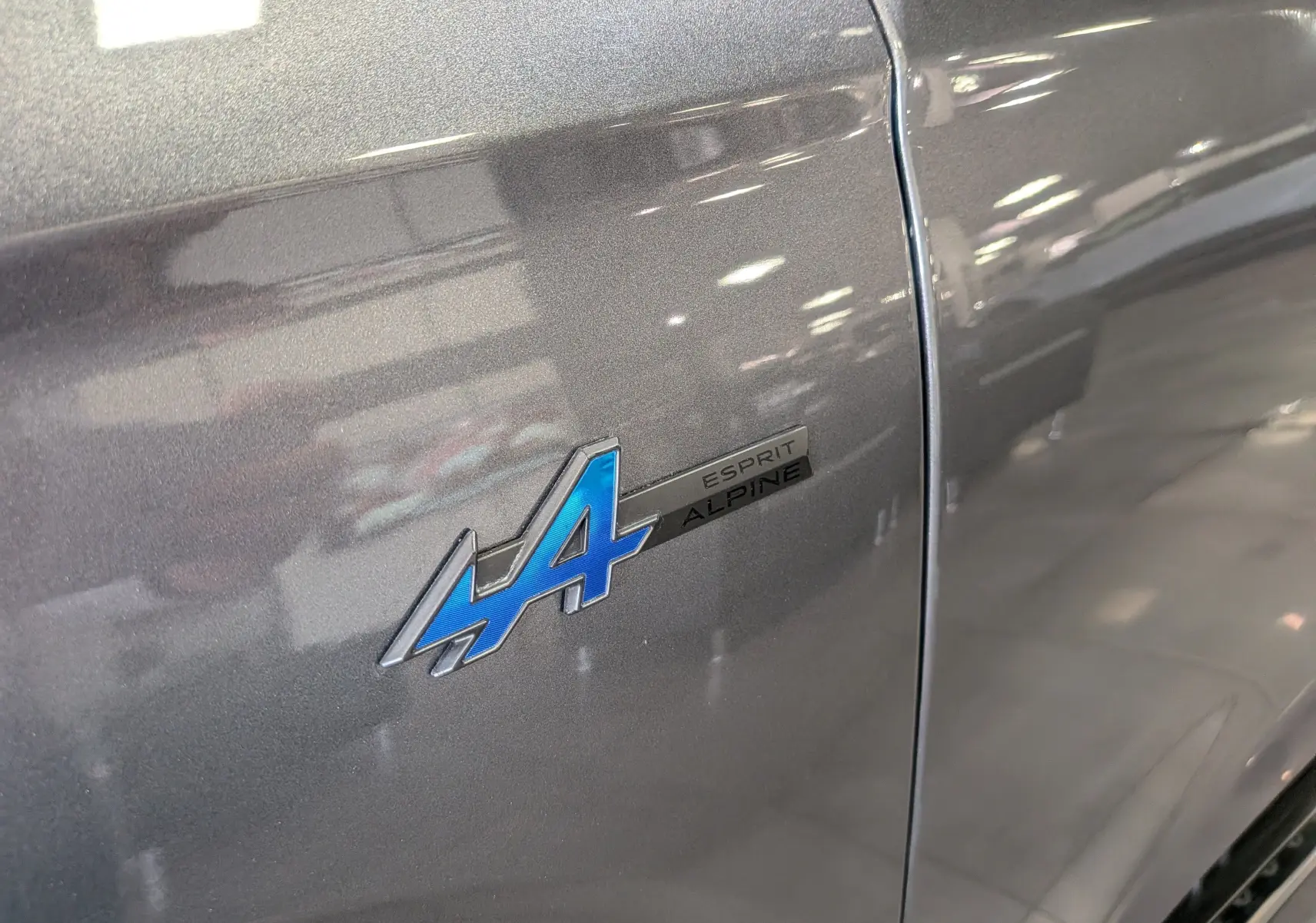 Gros plan sur l'écusson bleu "A Esprit Alpine" sur la porte gris schiste d'un Renault Austral 2023.