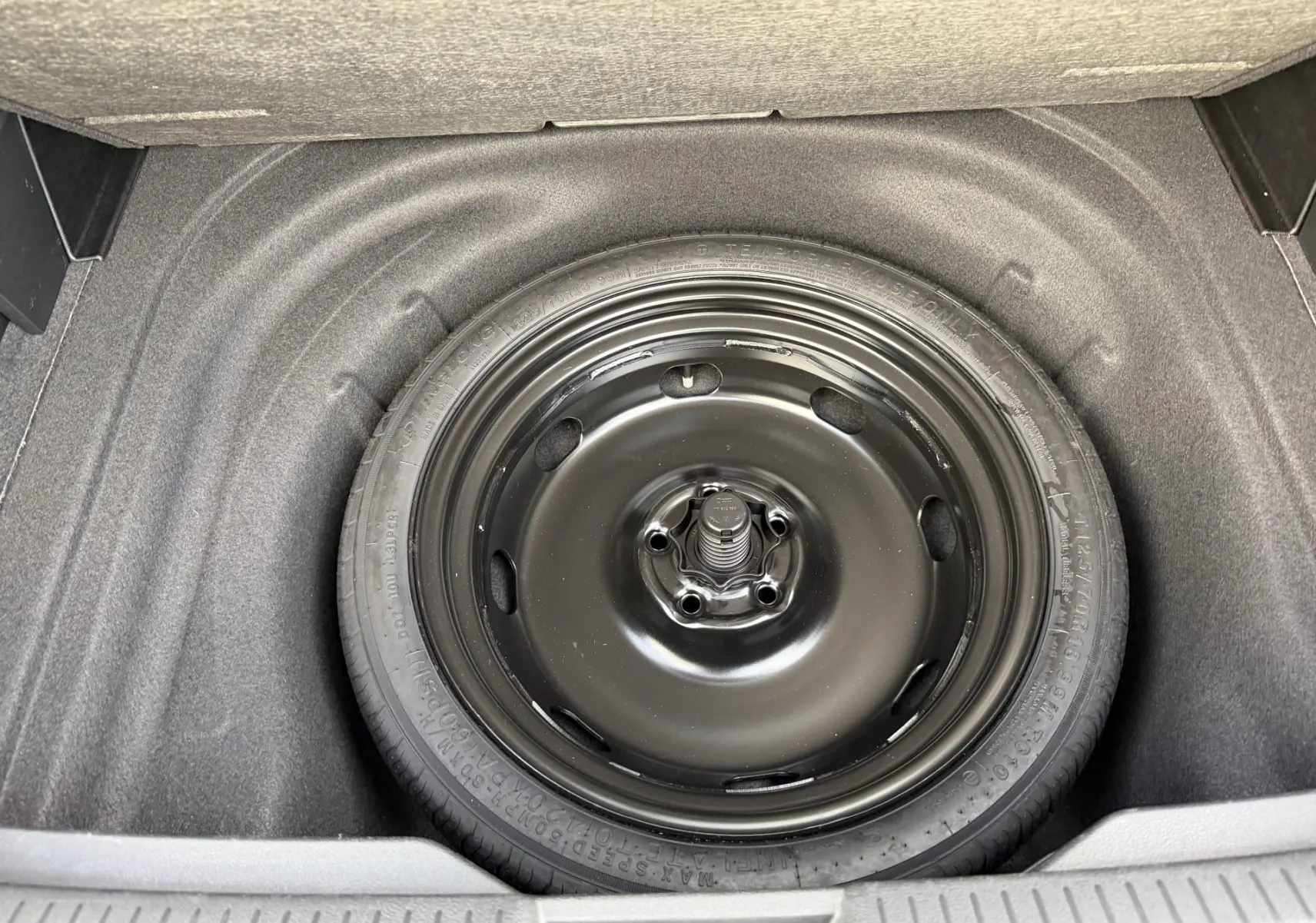 Gros plan sur la roue de secours compacte noire dans le coffre d’une Volkswagen Golf SW rouge.