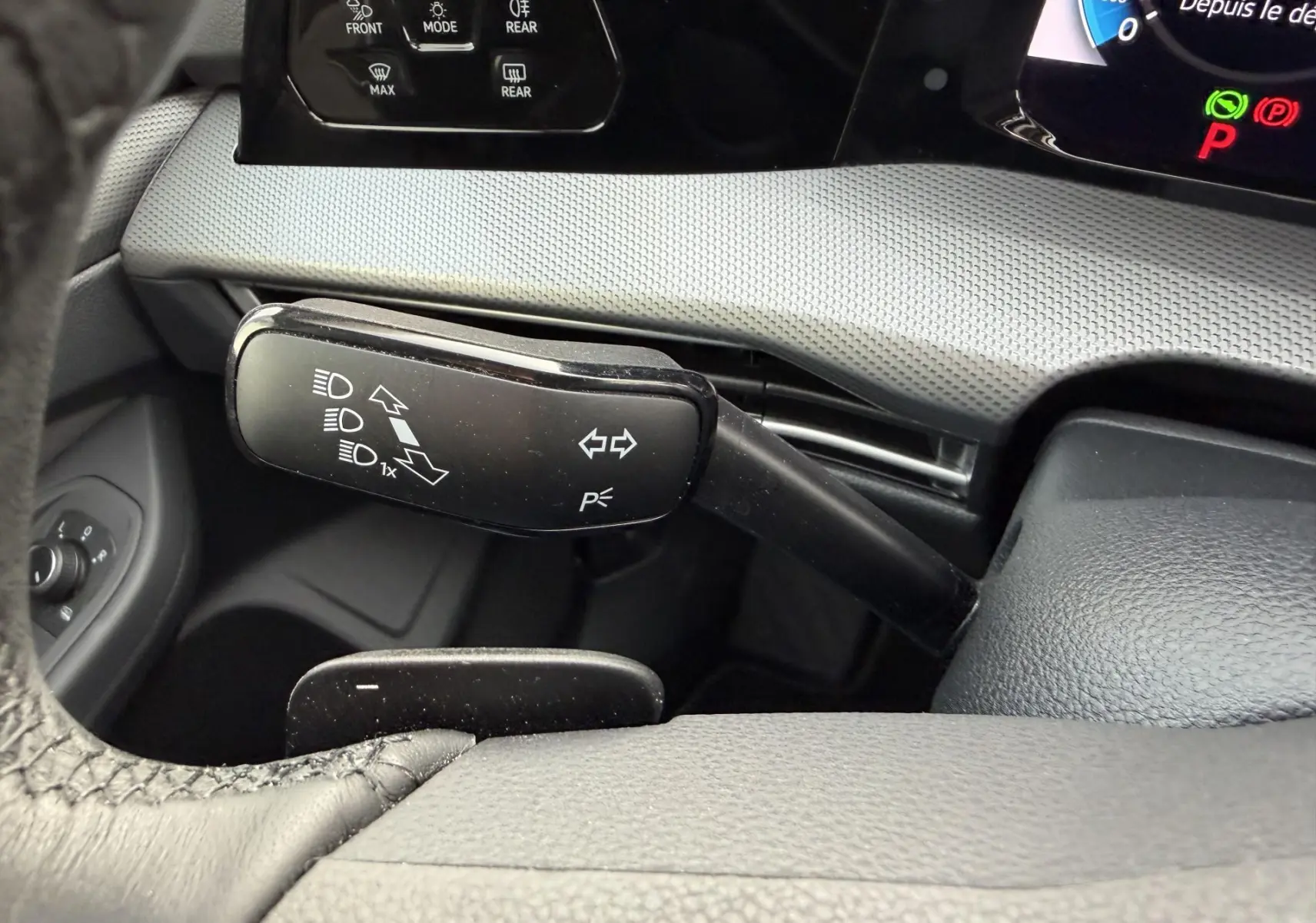 Gros plan sur la manette de clignotant noire à gauche du volant dans l’habitacle gris d’une Volkswagen Golf SW rouge.
