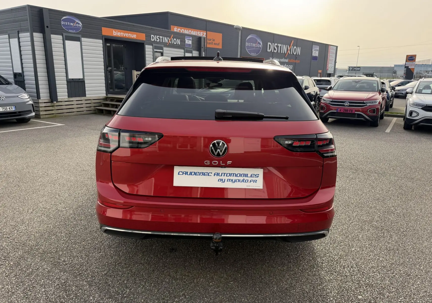 Vue arrière d'une Volkswagen Golf SW rouge avec attelage rabattable sur parking de concession.