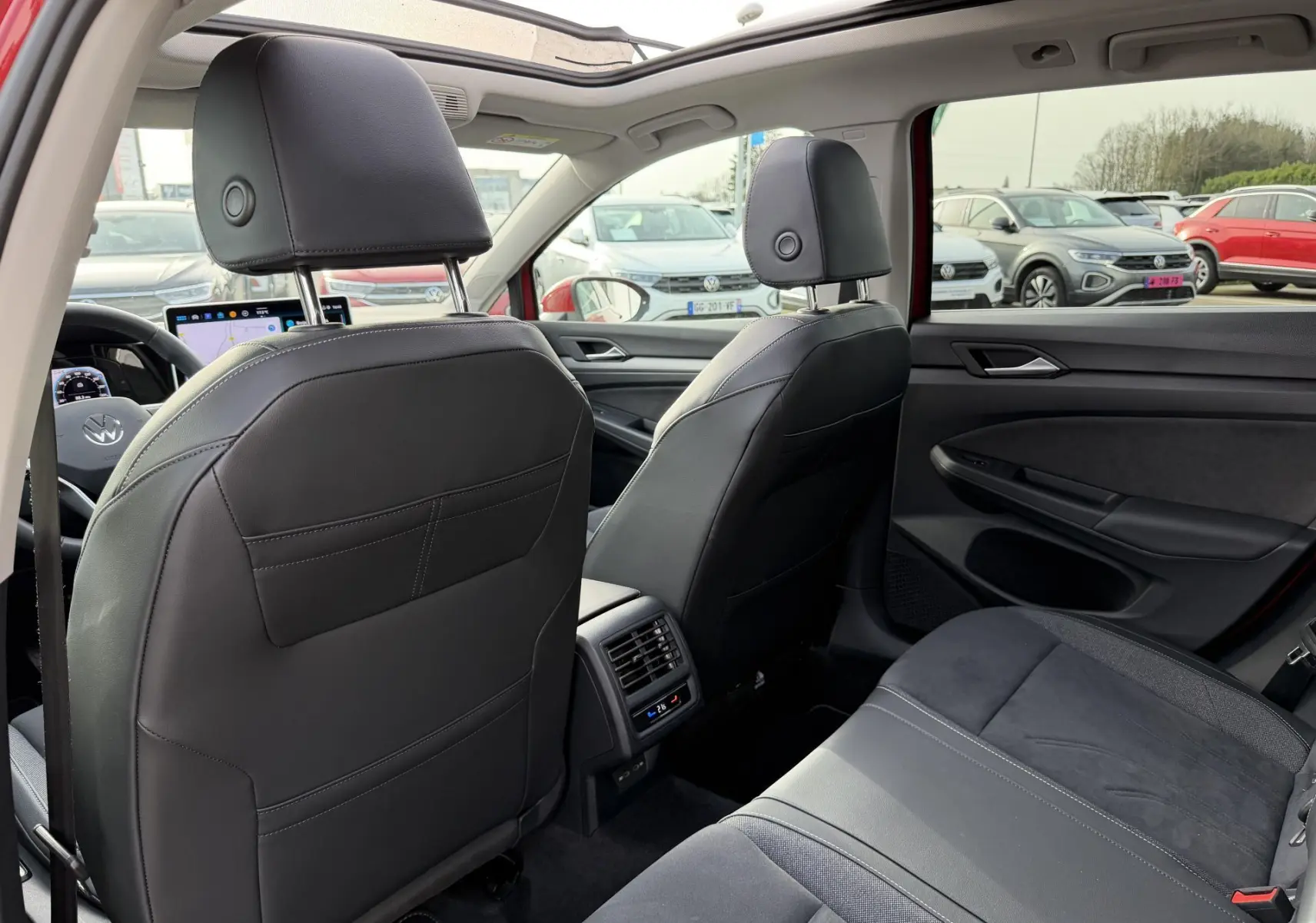 Vue intérieure arrière de la Volkswagen Golf SW rouge 2025, sièges en cuir noir et toit ouvrant panoramique visible.