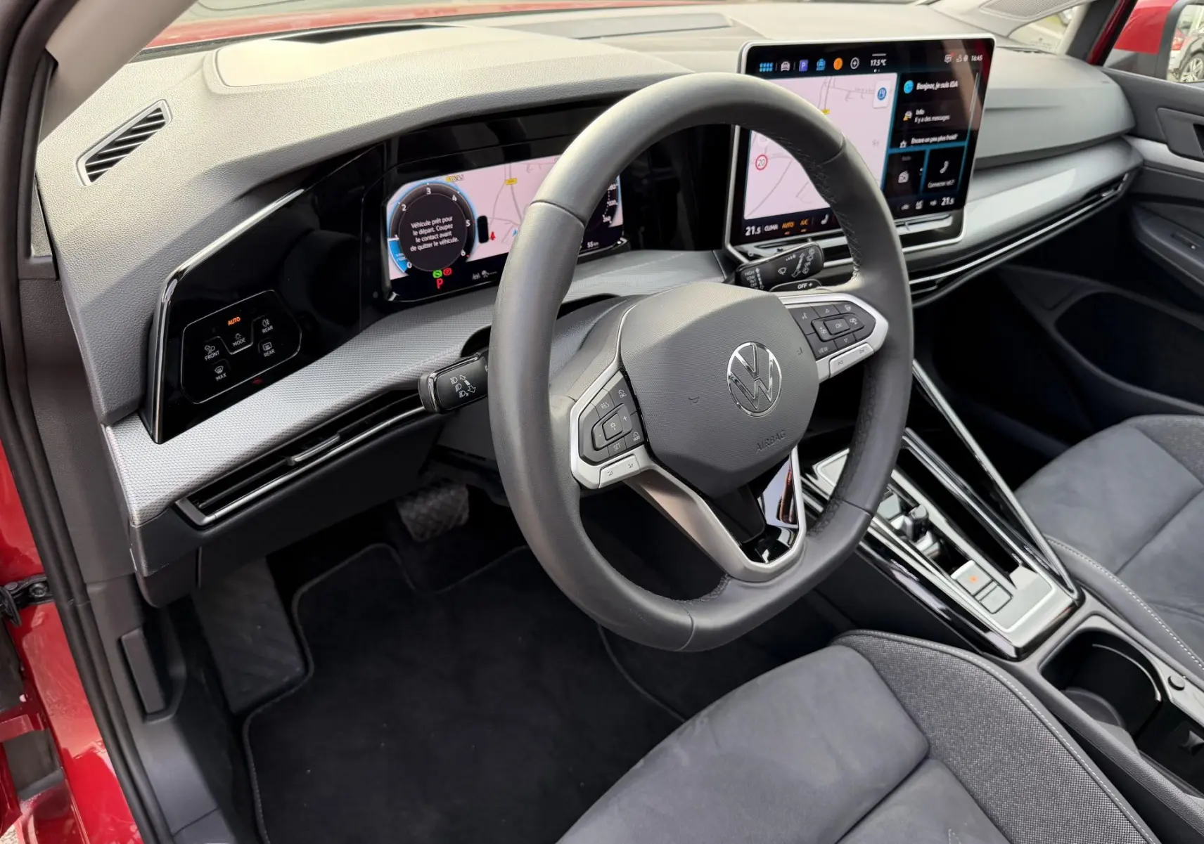 Vue intérieure côté conducteur de la Volkswagen Golf SW rouge 2025, volant multifonction et écran tactile central visible.