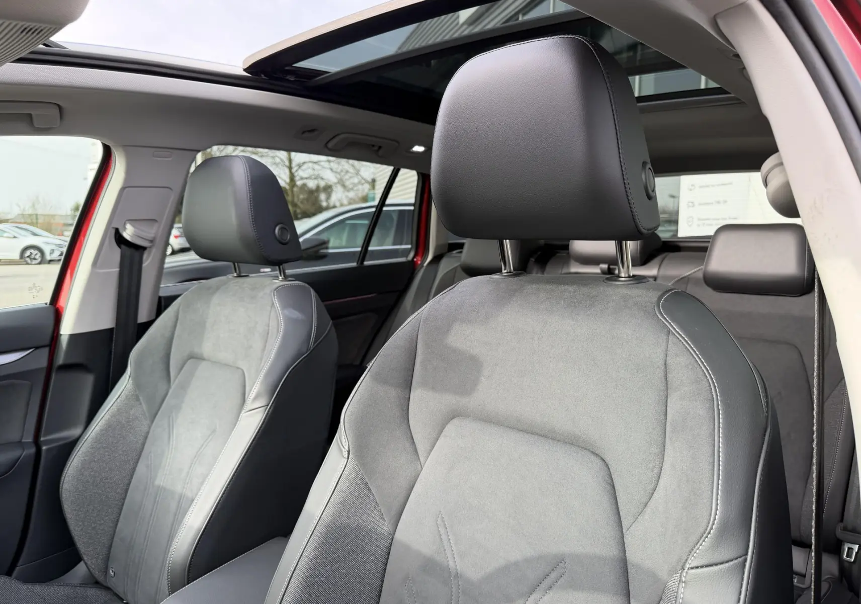 Vue intérieure côté avant droit du siège conducteur en tissu et cuir gris dans une Volkswagen Golf SW rouge avec toit ouvrant panoramique.