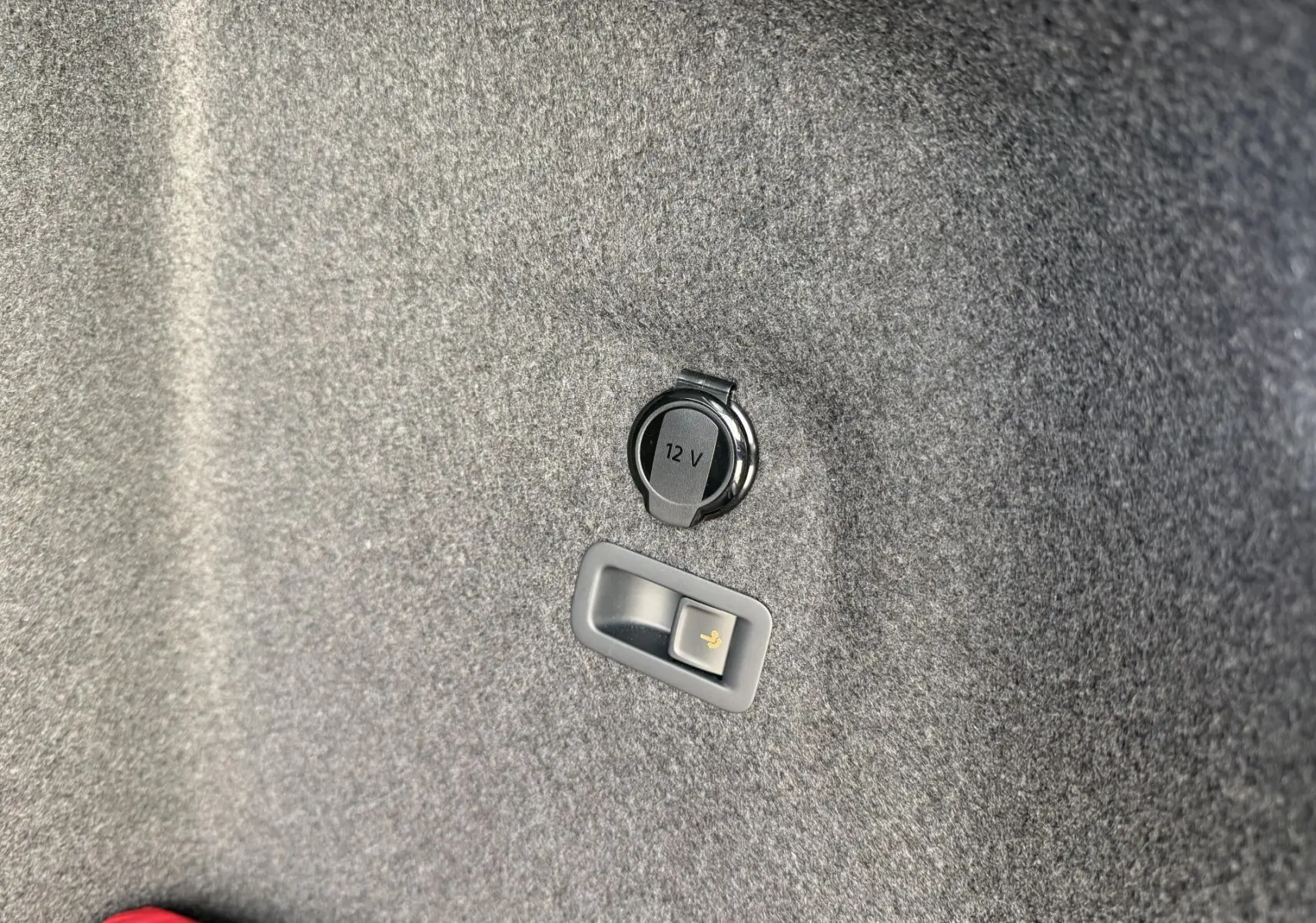 Détail de la prise 12V et levier de déverrouillage électrique de l'attelage dans le coffre de la Volkswagen Golf SW rouge.