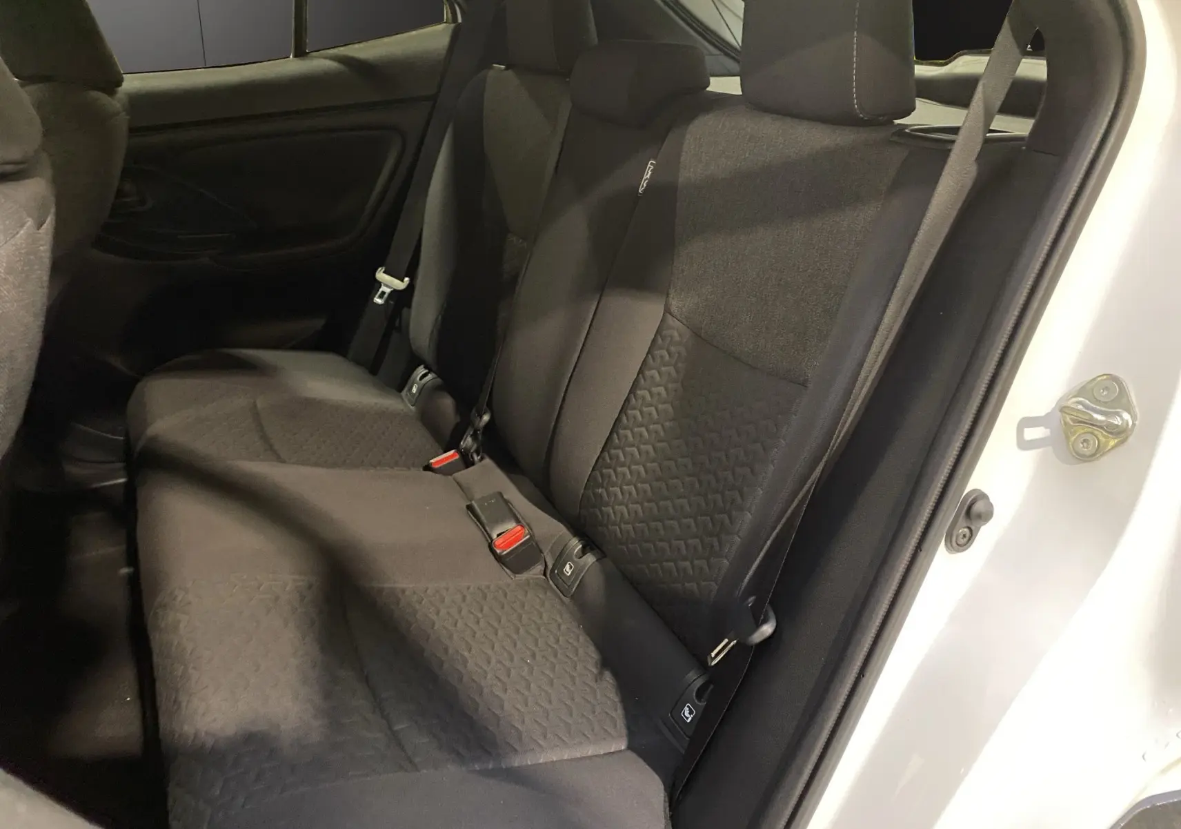 Vue latérale intérieure des sièges arrière noirs en tissu du Toyota Yaris Cross blanc, porte arrière ouverte.