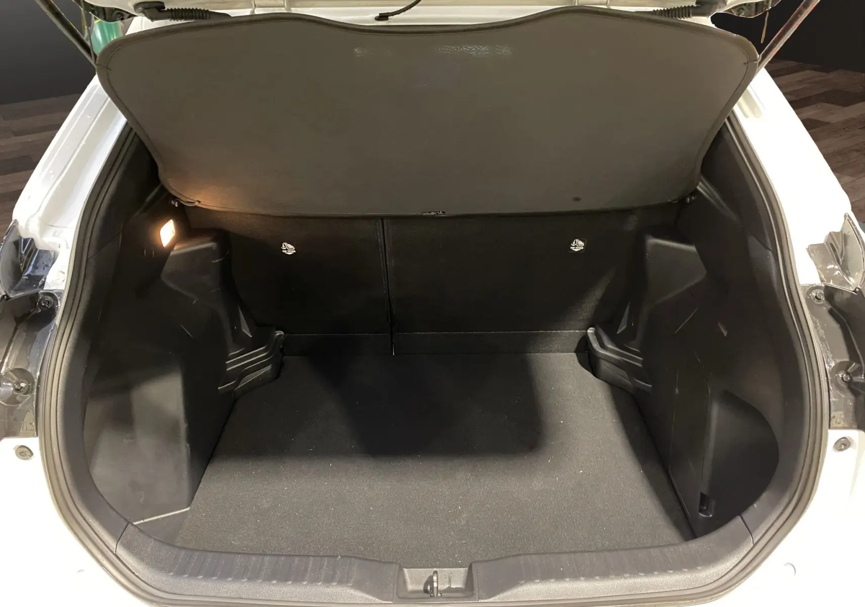 Coffre ouvert vu de l'arrière d'une Toyota Yaris Cross blanche, espace de chargement propre et éclairé.