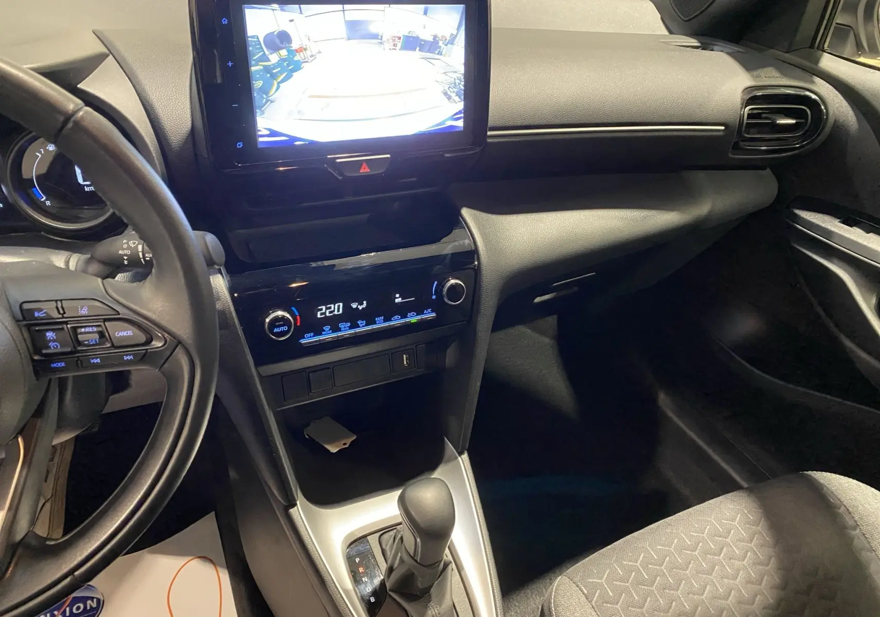 Intérieur noir de la Toyota Yaris Cross 116H, vue du tableau de bord côté conducteur avec écran tactile et caméra de recul affichée.