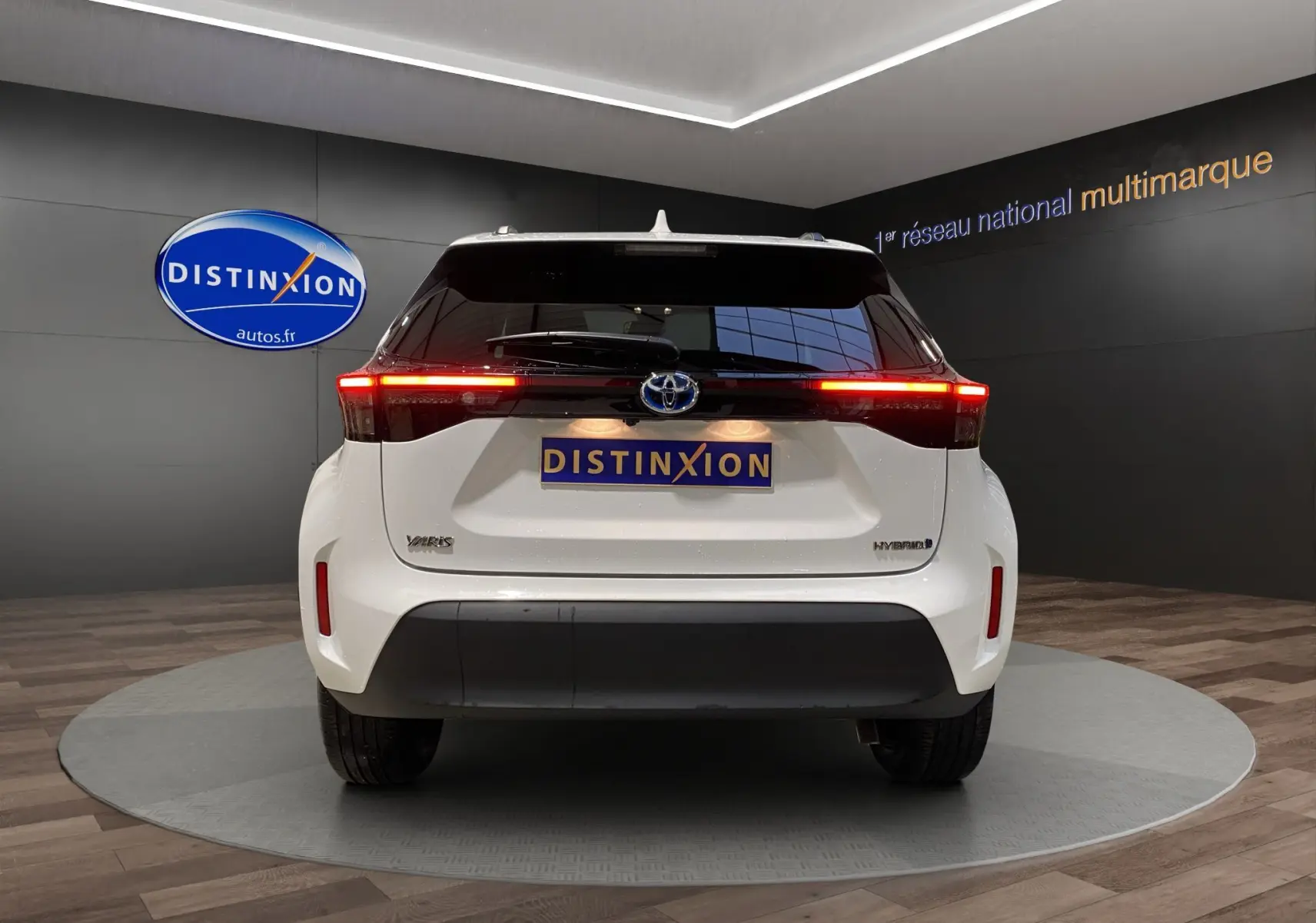 Vue arrière d'une Toyota Yaris Cross blanche hybride avec feux LED allumés dans un showroom.