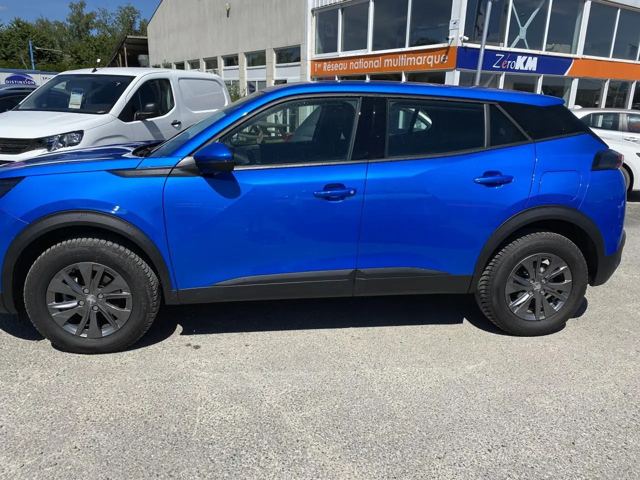 Profil côté gauche d'un Peugeot 2008 bleu Vertigo 2021 avec jantes alliage et protections noires sur les passages de roues.