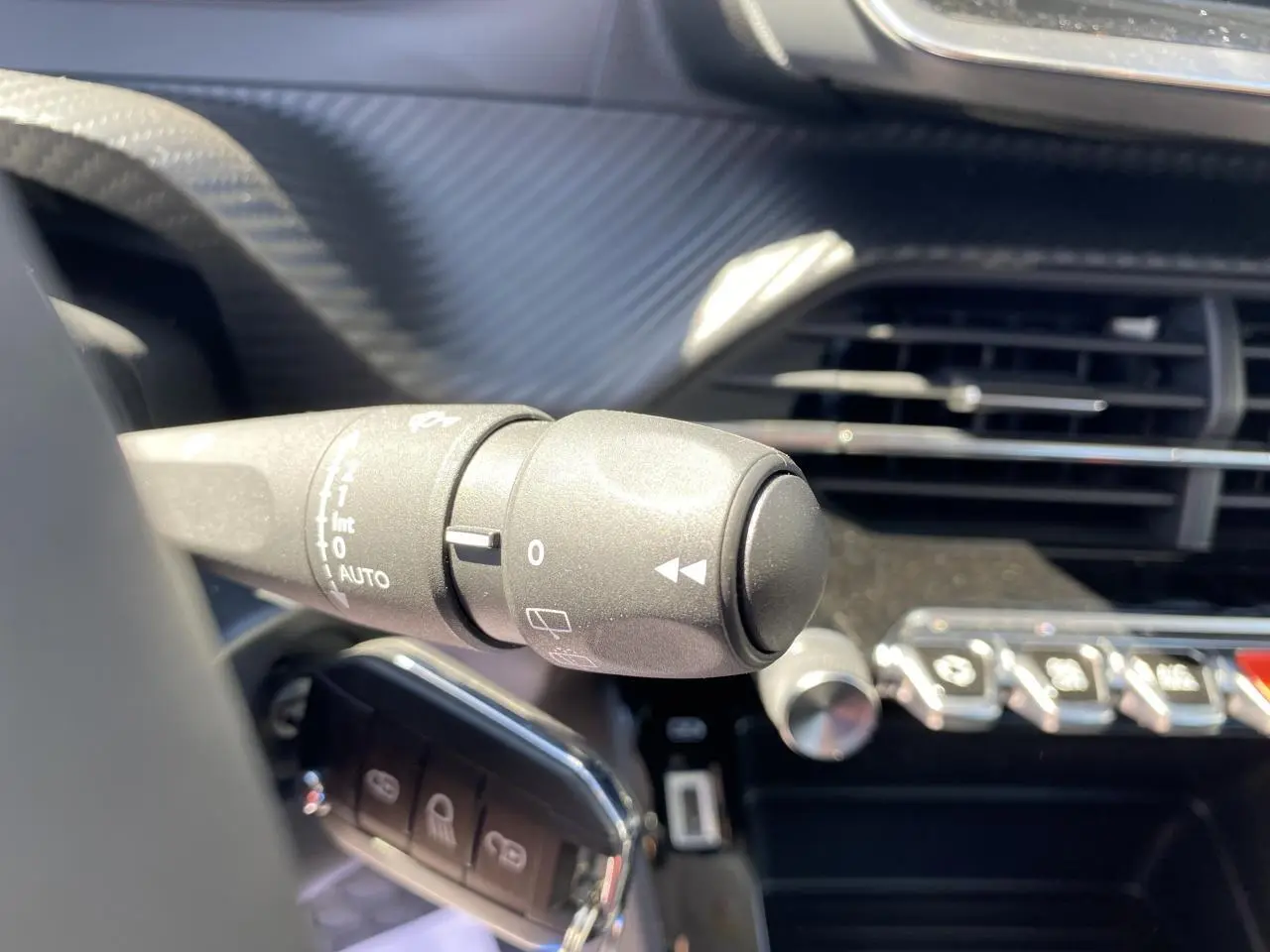 Gros plan sur la commande d'essuie-glace à gauche du volant dans l'habitacle sombre d'une Peugeot 2008 bleu Vertigo.