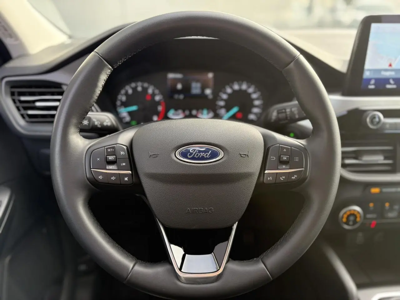 Vue rapprochée du volant multifonctions en cuir noir du Ford Kuga 2024 avec tableau de bord et écran GPS tactile visible.