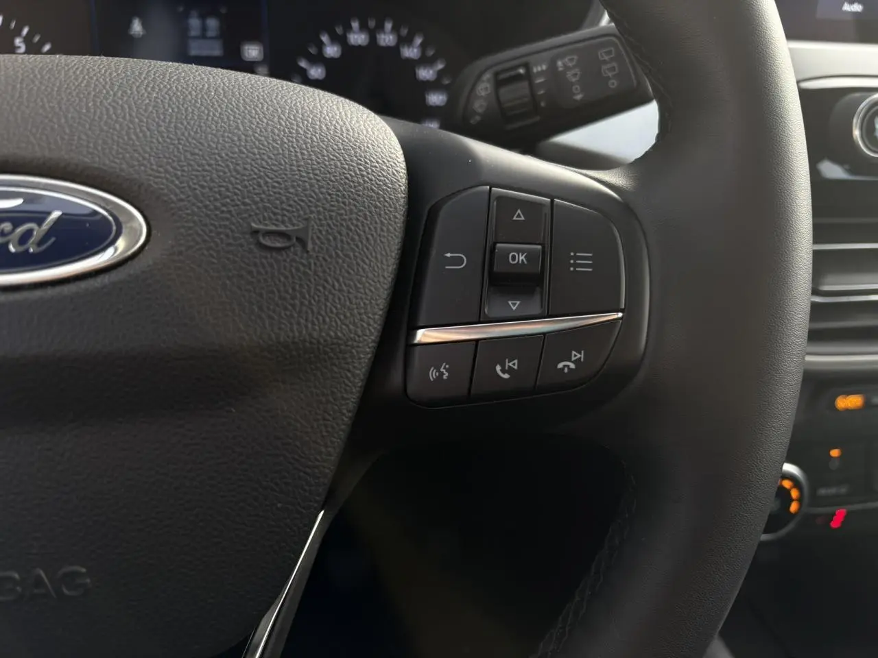 Gros plan sur le volant multifonctions en cuir du Ford Kuga 2024, montrant les commandes à droite et le logo Ford central.