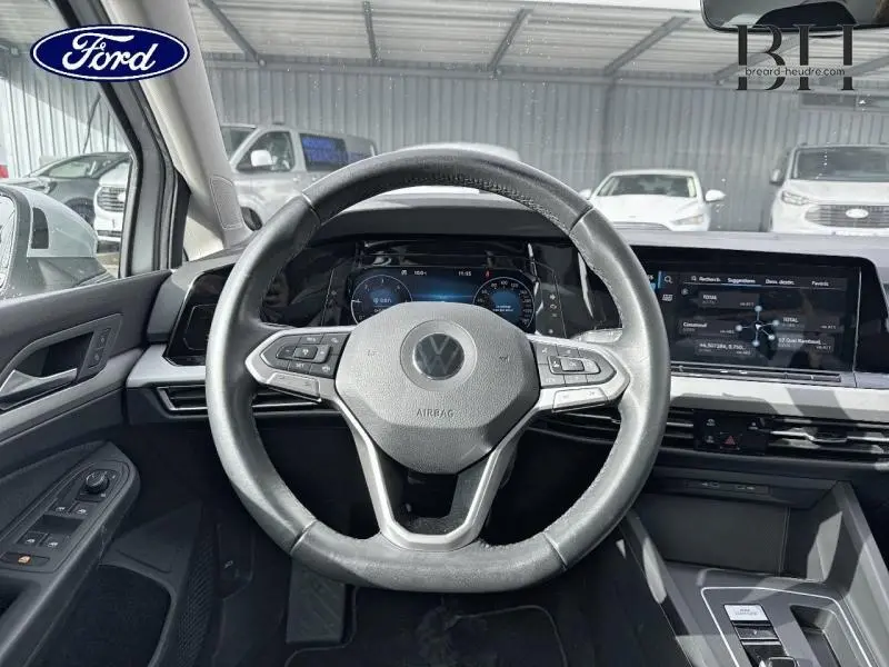 Vue intérieure centrée sur le volant cuir multifonction d'une Volkswagen Golf gris lunaire avec tableau de bord numérique et écran tactile.