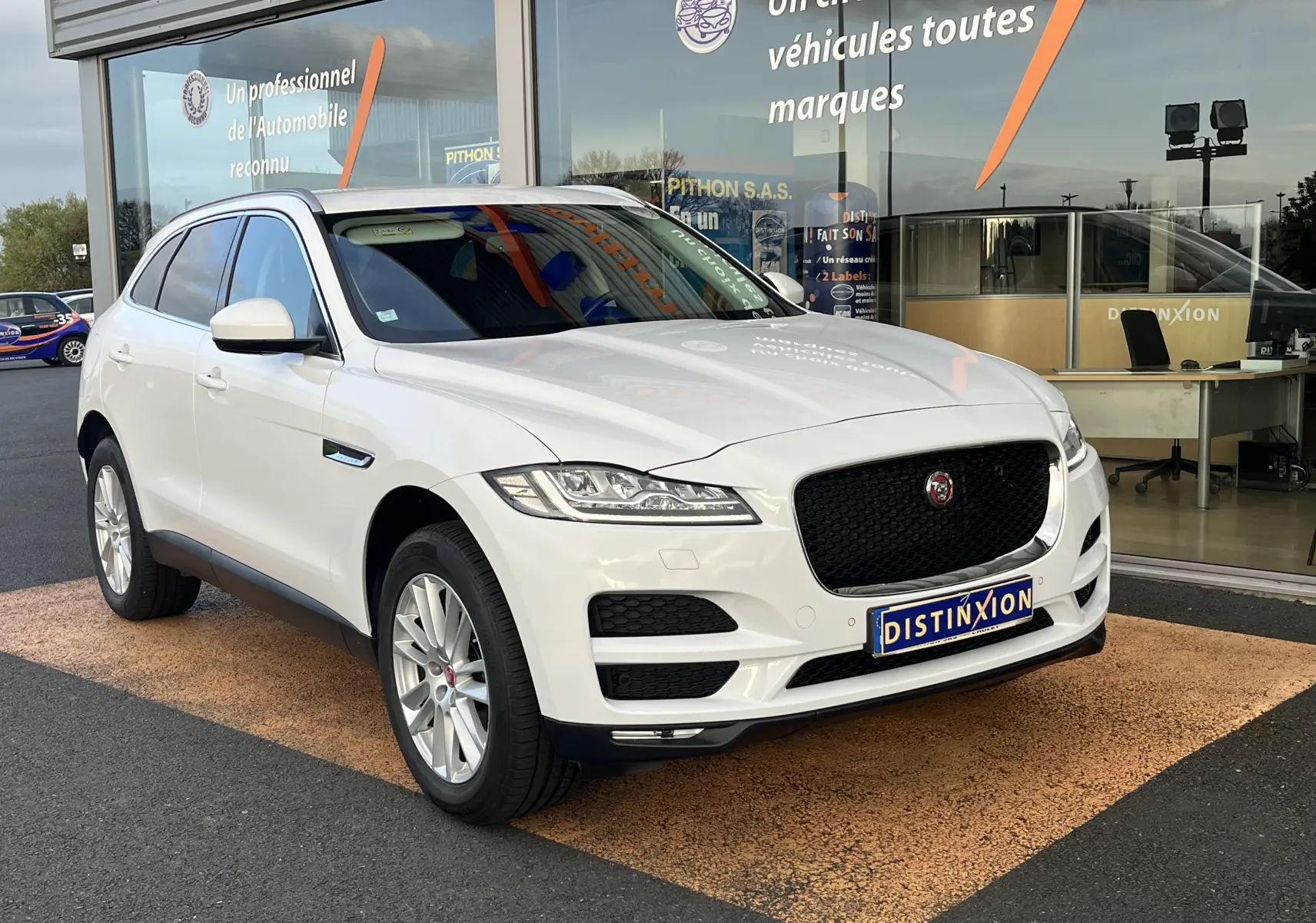 Jaguar F-PACE 240D Prestige blanc vue 3/4 avant droit devant un showroom avec calandre noire distinctive.