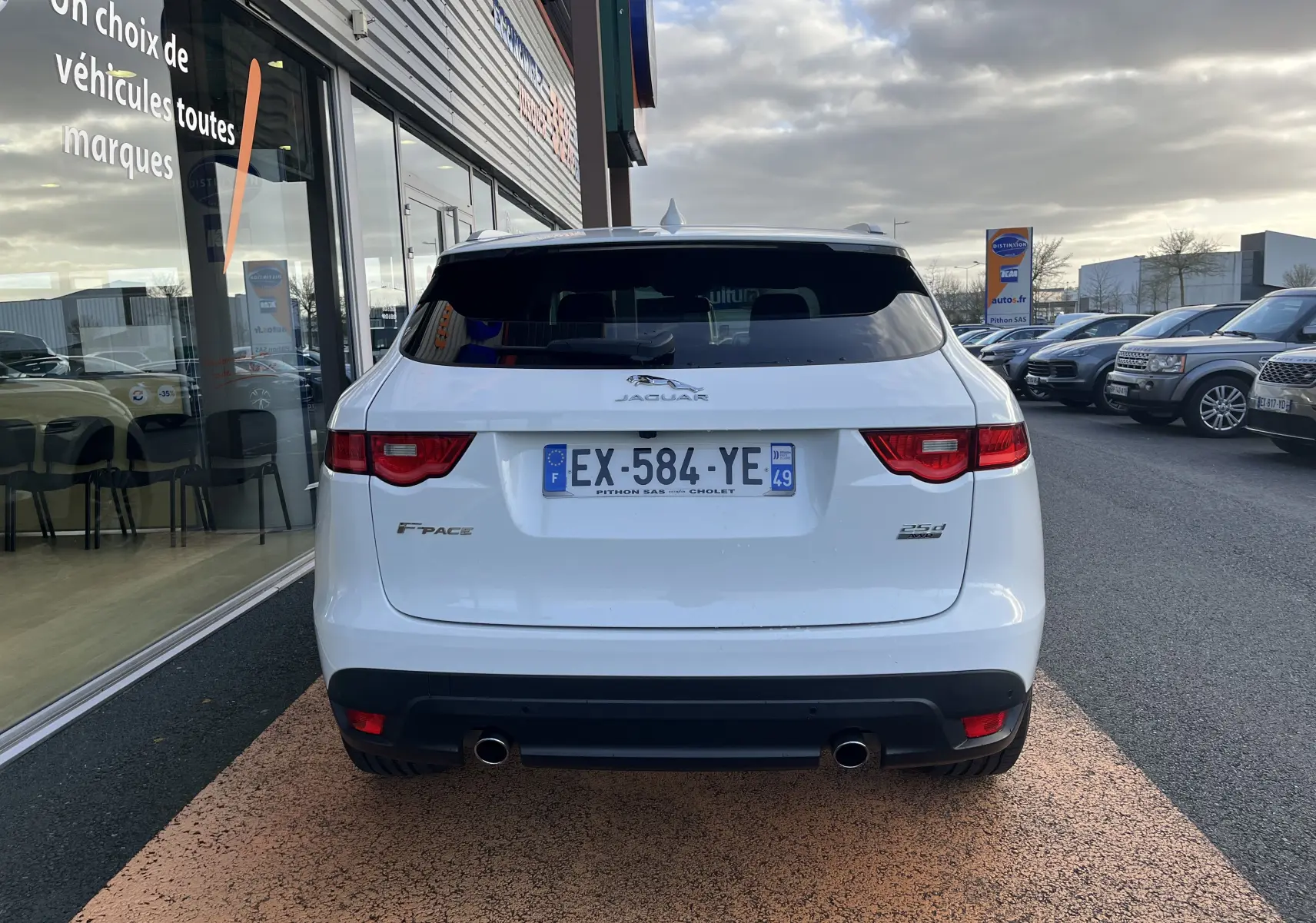 Vue arrière d'un Jaguar F-PACE blanc de 2018, avec double sortie d'échappement et feux arrière allumés.