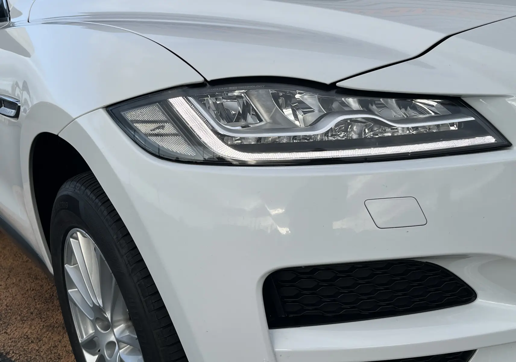 Gros plan sur l'avant gauche blanc d'une Jaguar F-PACE 240D Prestige 2018, mettant en valeur son phare LED et la jante alu.